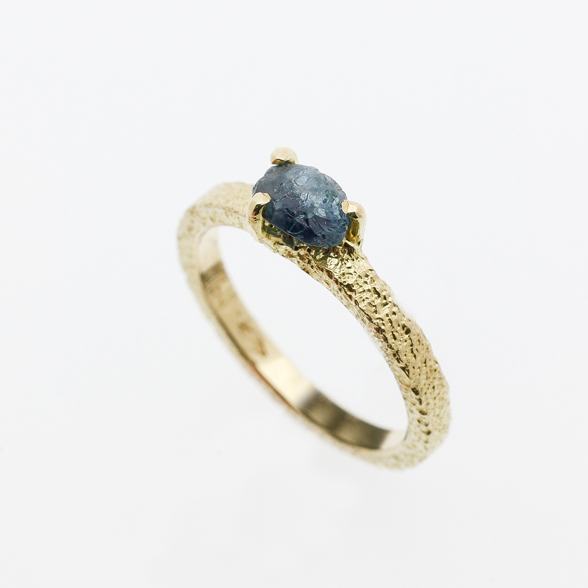 Yellow gold engagement ring with a rough sapphire in a solitaire.